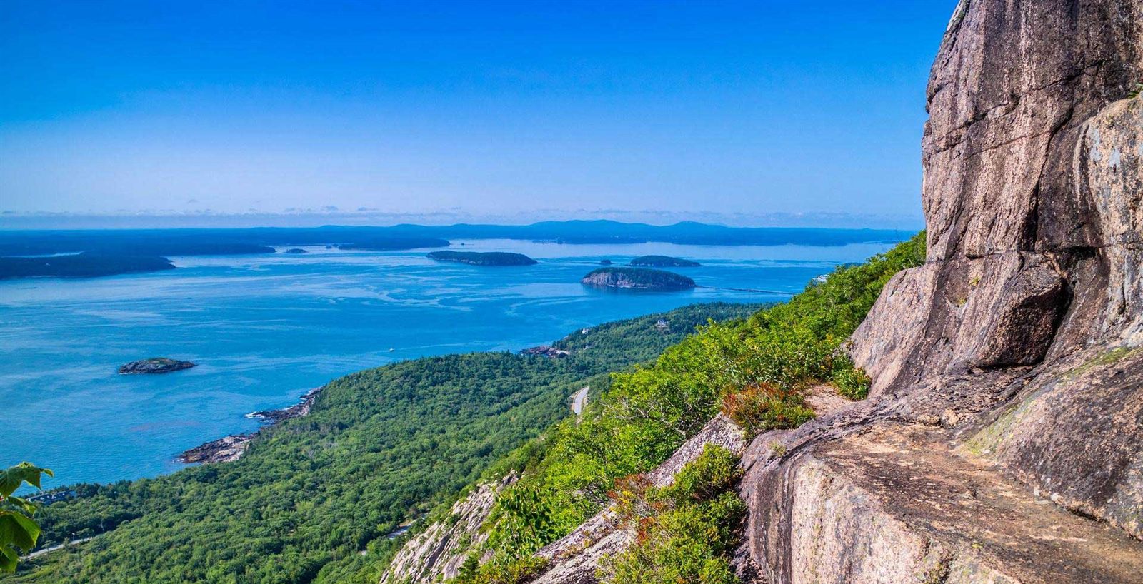 Granite cliff and forest above islands in a blue bay on the coast of Maine