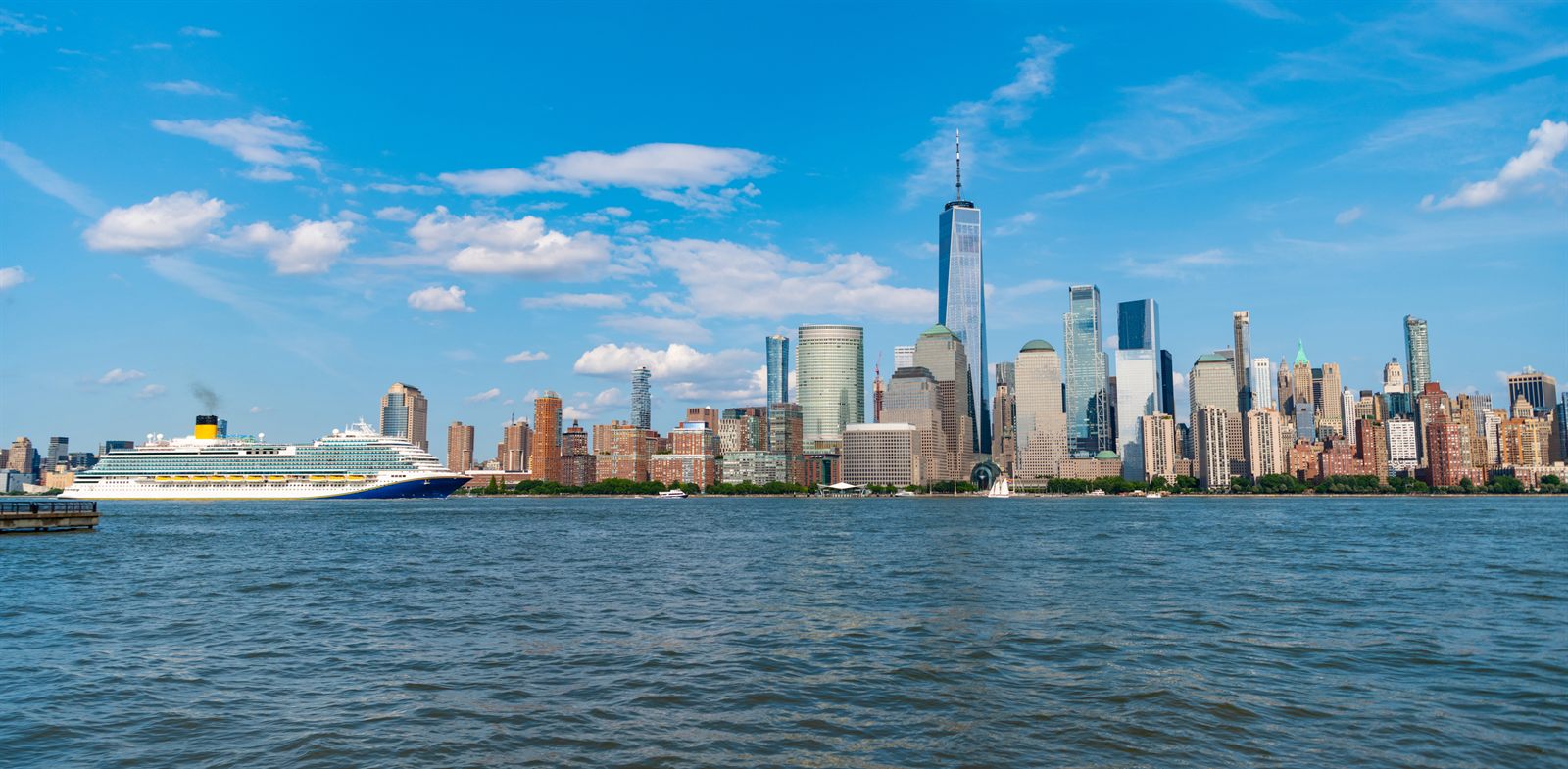 Cruise ship sailing past the Lower Manhattan skyline under a blue sky